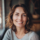 Femme souriante aux cheveux ondulés près d'une fenêtre.
